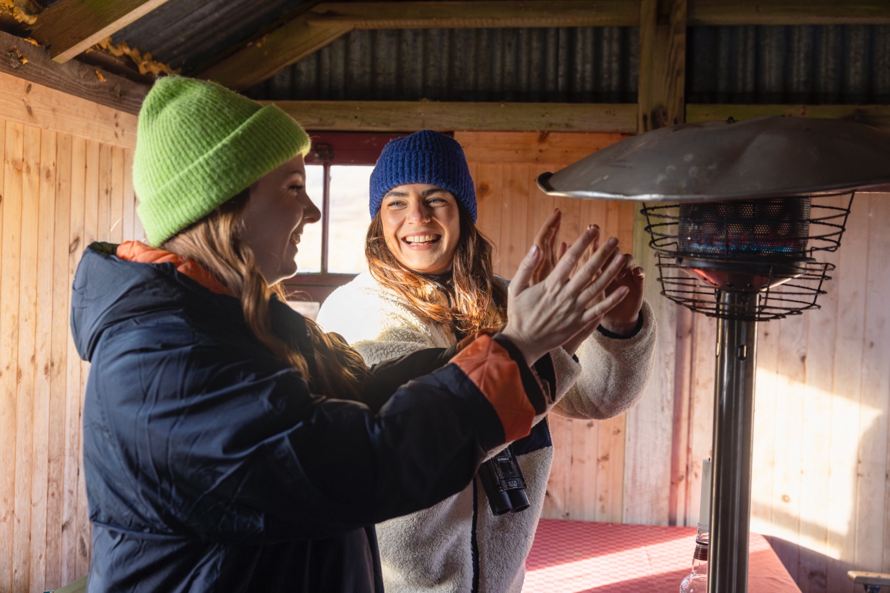 Friends warm their hands on a heater in a Bothy